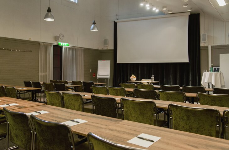 HS Dirigenten 730'480 1 Konferensrum med gröna stolar, träbord, projektionsskärm och blädderblock. Nödutgångsskylt synlig. Rum inrett för presentation. Hesselby Slott Hässelby nära Stockholm
